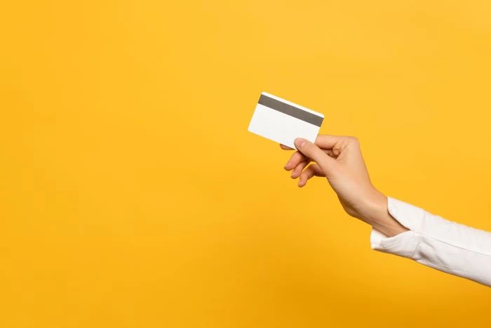 Hand over yellow background using a credit card to pay using a virtual terminal.