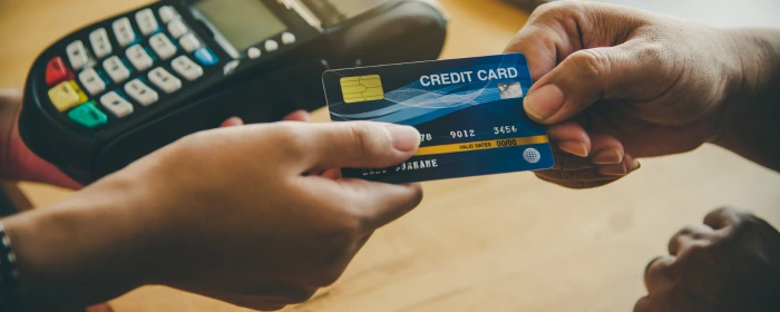 Two hands exchanging a card near a POS terminal at a business using credit card processing