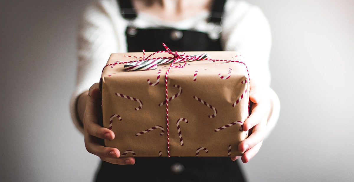 woman in black overalls holding a holiday gift with candy cane wrapping paper