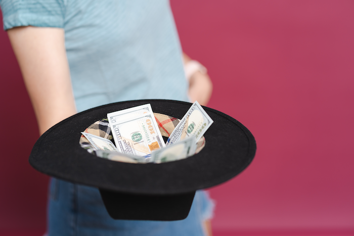 A person holding a black hat with currency inside it