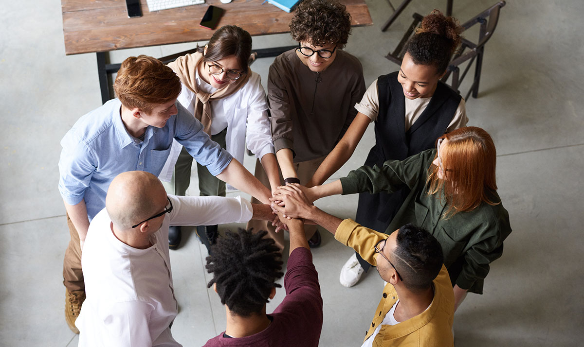 team of coworkers standing in a circle, each with one hand in the center 