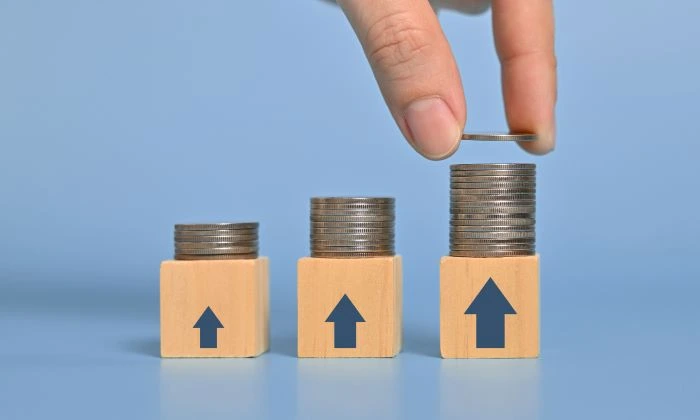 A person stacking merchant account fee coins on wooden blocks that have arrows pointing up. 