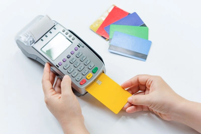 A person processes a payment by inserting a credit card inside a terminal with a pile of credit cards nearby. 